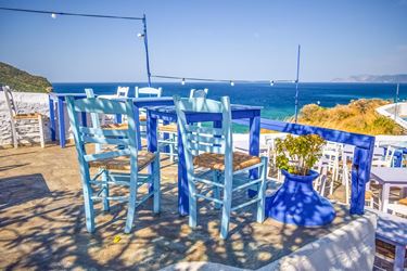 Γαλάζιες καρέκλες και τραπέζια σε αυλή ταβέρνας με θέα στη θάλασσα