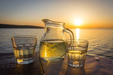 Κανάτα και ποτήρια με κρασί πάνω σε τραπέζι δίπλα στη θάλασσα